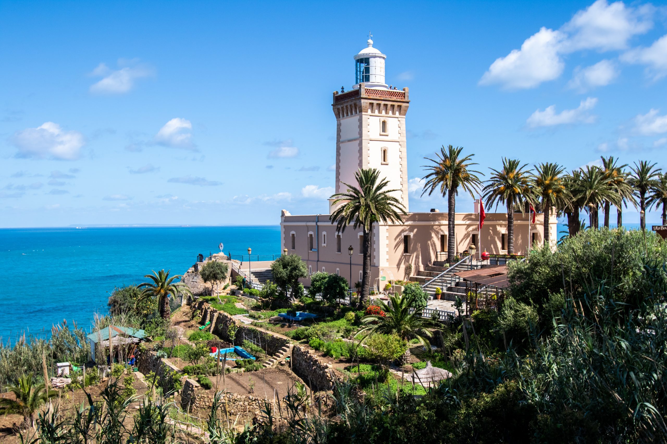 Cape Spartel lighthouse in Tangier with white tower and palm trees, surrounded by green gardens overlooking the blue ocean